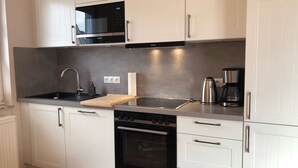 Une cuisine moderne avec des meubles blancs, un évier en acier inoxydable, un four à micro-ondes, une machine à café et un four.