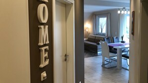 A modern interior with a 'HOME' sign on the wall, a dining area with a table and chairs, and a living room with a sofa and a window.