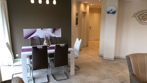 A modern dining area with a white table and chairs, a vase with dried flowers, and a pendant light fixture.