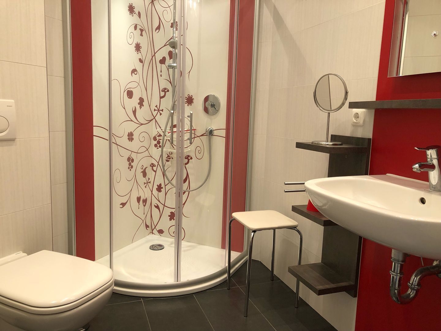 Et moderne badeværelse med et glasbadeværelsesafskærmning, et hvidt toilet, en lille skammel og en vask med et spejl.
