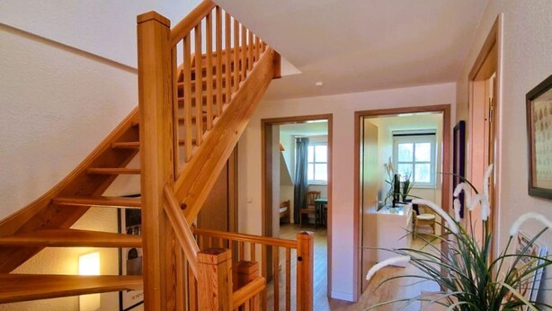 Eine Holztreppe führt zu einer zweiten Etage, eine Zimmerpflanze und ein Flur mit einer Tür zu einem weiteren Raum.