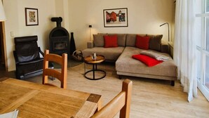 Ein Wohnzimmer mit einer Couch, einem Kamin, einem Esstisch mit Stühlen und einem Fenster mit Vorhängen.