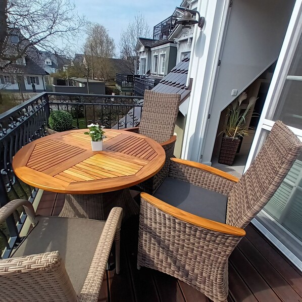 A balcony with wicker furniture, a round wooden table, and a potted plant.