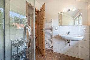 A bathroom with a glass shower enclosure, a white sink, and a wooden door.