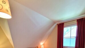 Une chambre à coucher avec un lit en bois, deux lampes de chevet, une fenêtre avec des rideaux rouges et un plafond en pente.