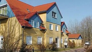 En række bolighuse med røde tage og gule vægge, beliggende i et boligområde med en asfalteret indkørsel.