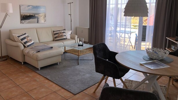 En moderne stue med sofa, sofabord og spisebord. Et maleri hænger på væggen, der er en gulvlampe, og der er udsigt ud ad vinduet.