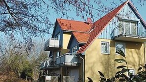 Et toetagers hus med rødt tag, balkon på øverste etage og en indhegnet have.