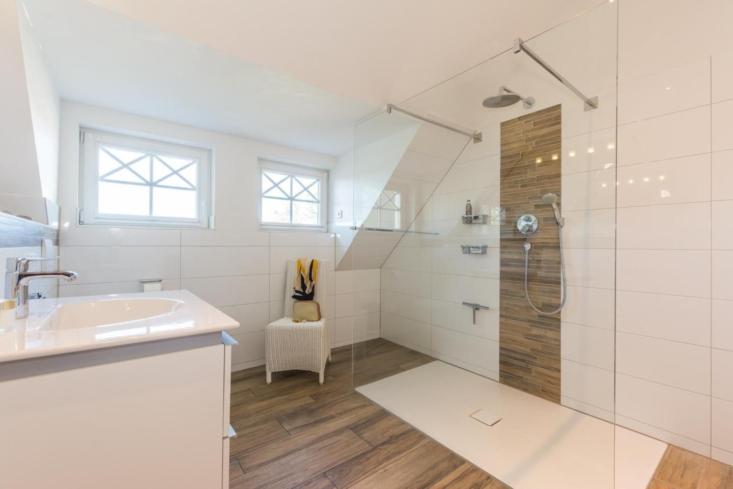 Ein modernes Badezimmer mit Dusche, Waschbecken und einem Sessel. Fenster mit Kreuzbleiglasur und Holzboden.