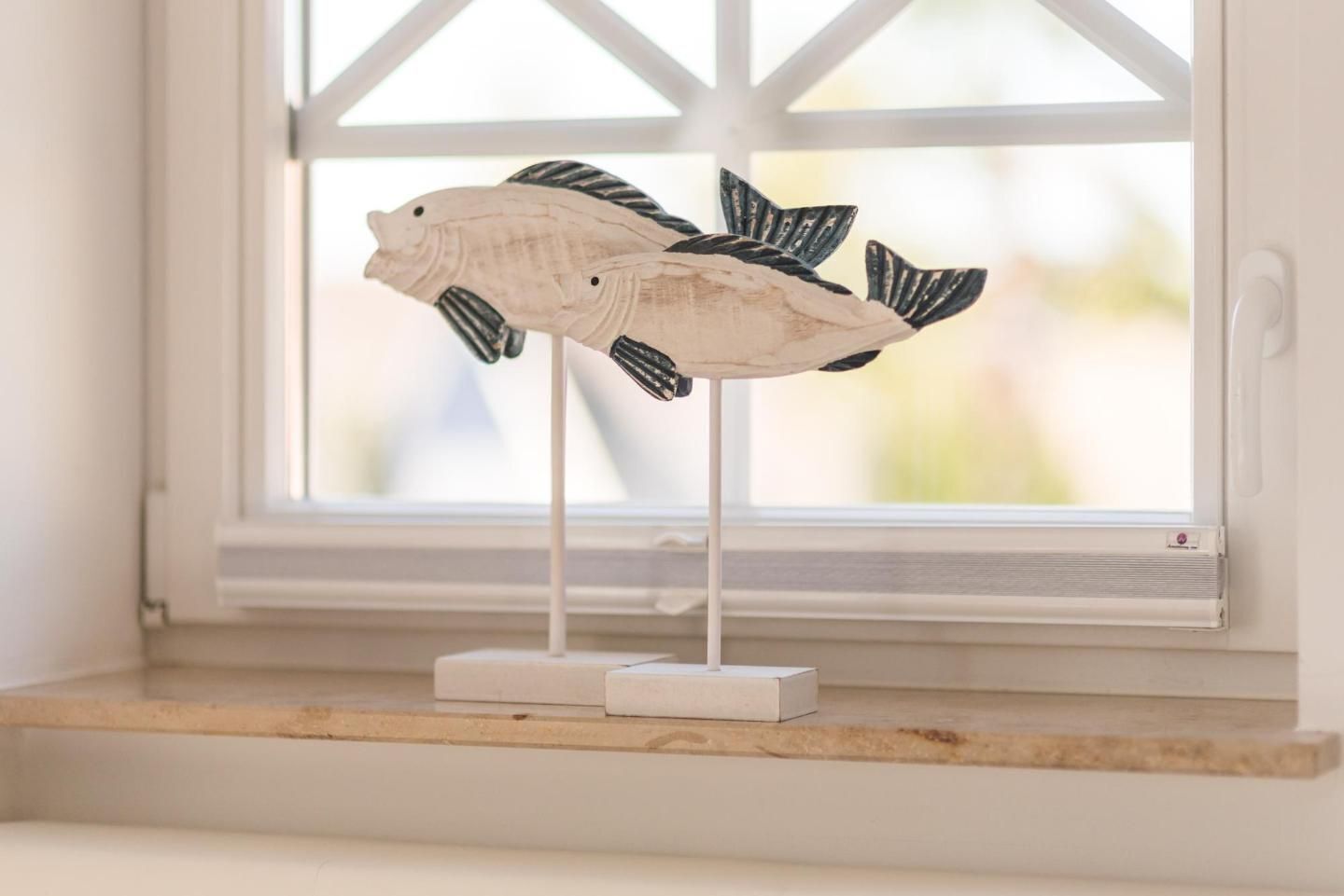 A white fish-shaped decoration on a shelf by a window.