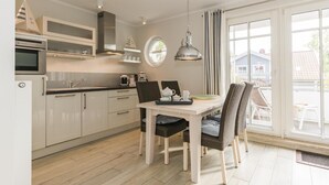 Una cocina moderna con armarios blancos, una mesa de comedor con sillas y vistas al exterior a través de amplios ventanales.