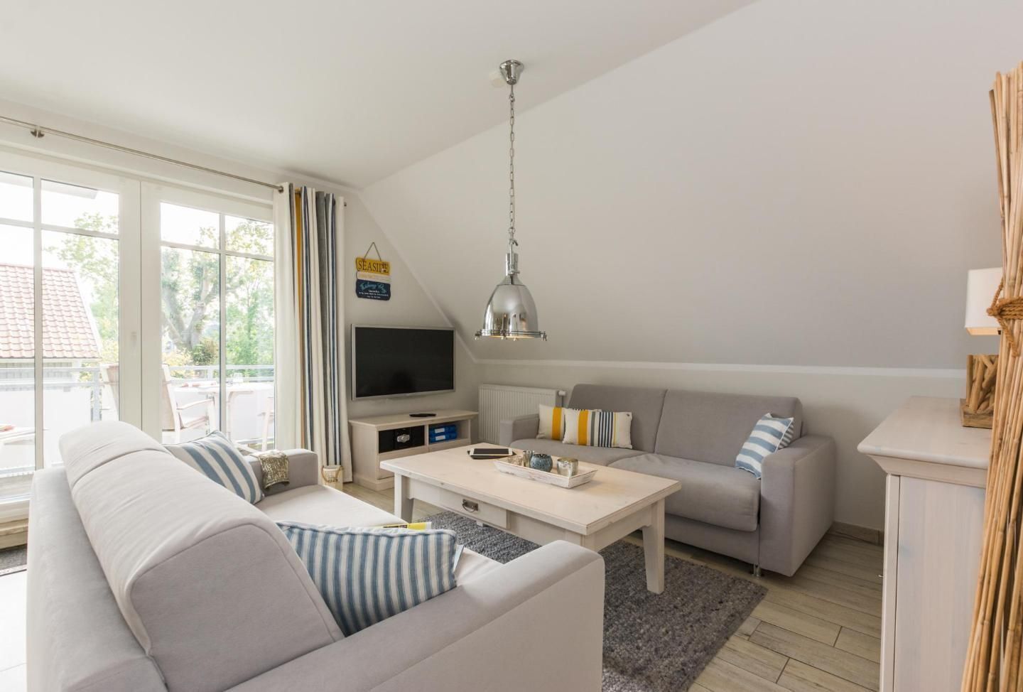 A modern living room with a sofa, a coffee table, a TV, and a hanging lamp.