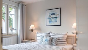 Un dormitorio ordenado con una cama, dos mesitas de noche, un ventanal con cortinas y una lámpara de pared.