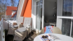 Un balcón con mobiliario de mimbre, una mesa con material de lectura y vista al interior.