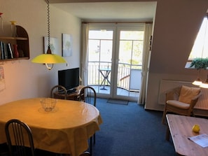 Uma sala de estar acolhedora com uma mesa redonda, televisão e varanda com uma cadeira.