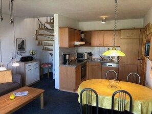 Cozinha compacta com armários de madeira, uma mesa de jantar com cadeiras e uma escada para um andar superior.