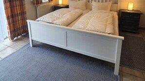 Una camera da letto con un letto bianco, due comodini con lampade, tende a quadri e un tappeto testurizzato.