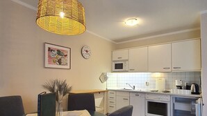 Una cucina compatta con mobili bianchi, un forno a microonde, un forno e un frigorifero. C'è un tavolo da pranzo con sedie e un lampadario.