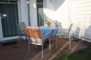 A patio with a table and four chairs, a potted plant, and a window with curtains.