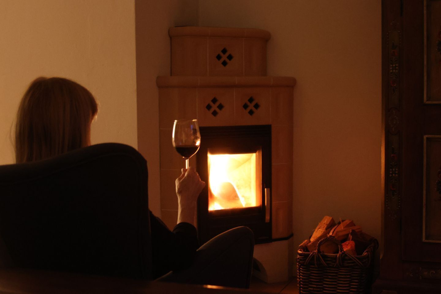 A person sitting by a fireplace with a glass of wine, a basket of bread, and a framed picture on the wall.
