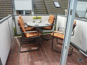 A patio with a round table and four chairs, a small potted plant, and a window with a view of a house.