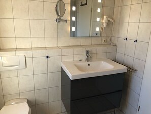 Une salle de bain avec un lavabo blanc, un miroir et des toilettes.