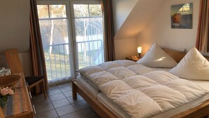 Una camera da letto con un letto grande, una scrivania e una sedia. Si vede una finestra con tende, una lampada sul comodino e un quadro appeso al muro.