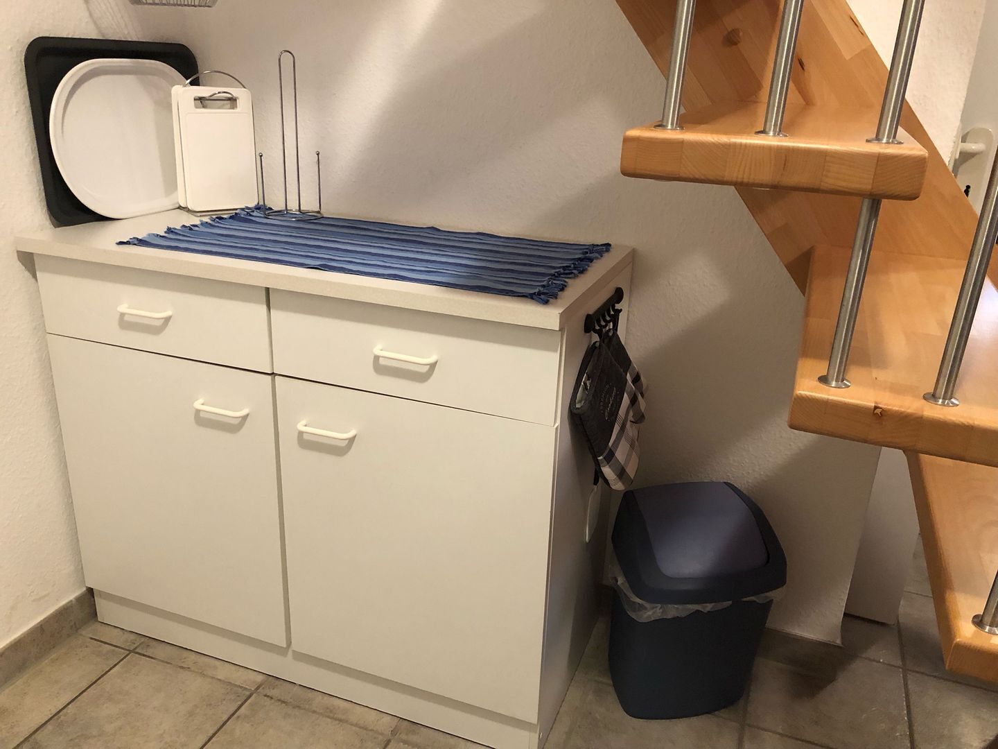 A kitchenette with a microwave, a kettle, a coffee maker, a trash bin, and a wooden chair.