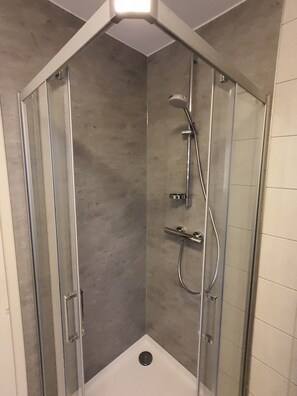 Lasiseinöillä varustettu suihkukaappi, jossa on suihkupää, käsisuihku ja käsisuihkuhana.