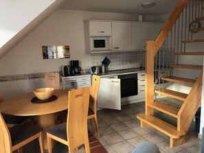 Moderni keittiö, jossa on valkoiset kaapit, sisäänrakennettu uuni ja puinen ruokapöytä tuoleineen.