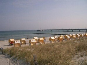 A beach with rows of wooden beach chairs and a pier in the background.