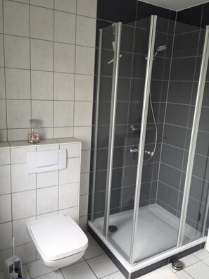 A bathroom with a glass-enclosed shower, a toilet, and a small shelf with a glass jar.