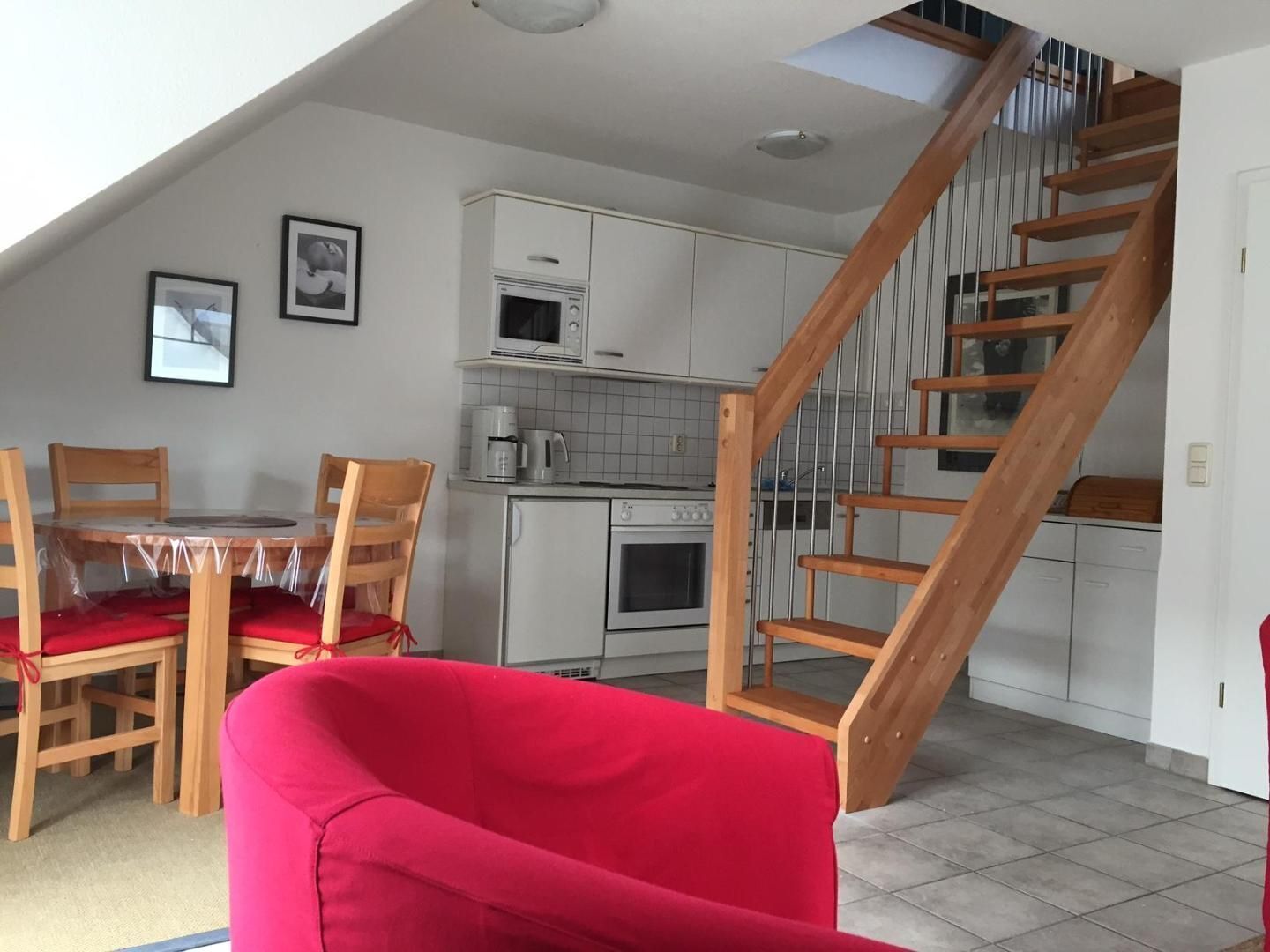 A modern kitchen with white cabinets, a microwave, and a stove. There is a wooden staircase leading to an upper level.