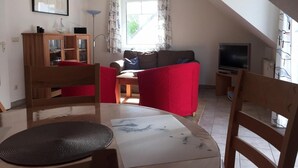 Un accogliente soggiorno con un divano, poltrone, una TV e un tavolo da pranzo.