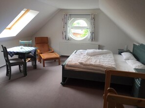 A bedroom with a bed, a chair, a table, and a window with a view.