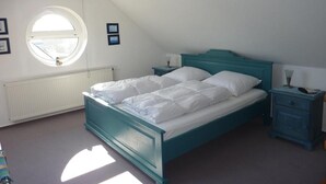Una camera da letto con un letto singolo, un comodino, una cassettiera, una finestra e un termosifone.