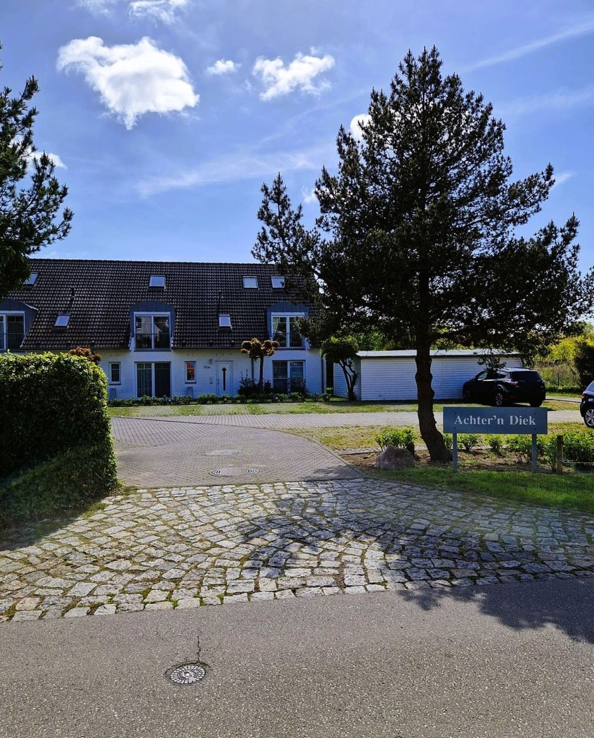 En bostadsbyggnad med en asfalterad uppfart, en skylt med texten ”Achter’n Diek” och en parkerad bil.