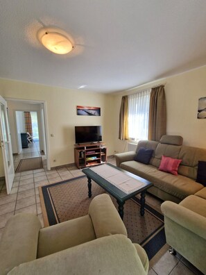 A living room with a sofa, a coffee table, a television on a stand, and a painting on the wall. - Darßer Weg 36 Whg. 9 - Holiday apartment near the beach (Zingst)
