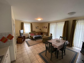 Ein Wohnzimmer mit einer Couch, einem Esstisch mit Stühlen, einem Fernseher und einer Küchenzeile mit Herd.