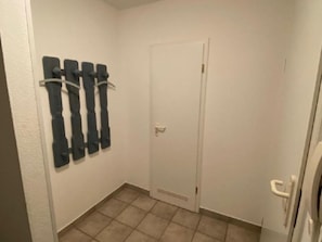 Ein schmaler, kleiner Flur mit einer weißen Tür und einem an der Wand befestigten Träger mit vier schwarzen Gegenständen.