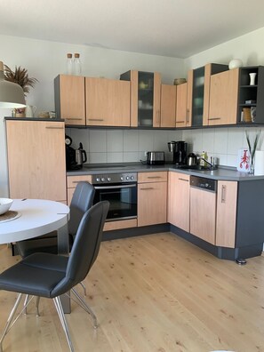 Una cocina moderna con armarios de madera clara, encimera negra, electrodomésticos de acero inoxidable y una mesa de comedor redonda con sillas negras.