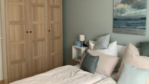 Ein Schlafzimmer mit Bett, Kissen, einem Nachttisch, einem Gemälde und einem Kleiderschrank.