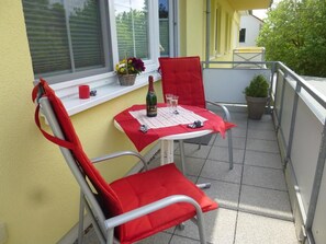 A small balcony with two red chairs and a table set for two, featuring a bottle and glasses. - Hafenstrasse 28 Whg. 3 - Lovingly furnished, sun-drenched 3-room apartment (Zingst)