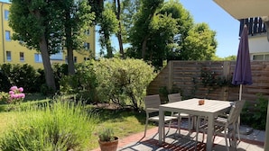A patio with a table and chairs, surrounded by a garden with various plants and a wooden fence. - Martha-Müller-Grählert-Weg 7/8 Whg.6 - Very nice, friendly and modern (Zingst)