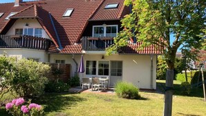 A two-story house with a red-tiled roof, a balcony, and a garden with pink flowers. - Martha-Müller-Grählert-Weg 7/8 Whg.6 - Very nice, friendly and modern (Zingst)