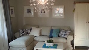 A living room with a sectional sofa, a white coffee table with a plant, a chandelier, and framed pictures on the wall. - Martha-Müller-Grählert-Weg 7/8 Whg.6 - Very nice, friendly and modern (Zingst)