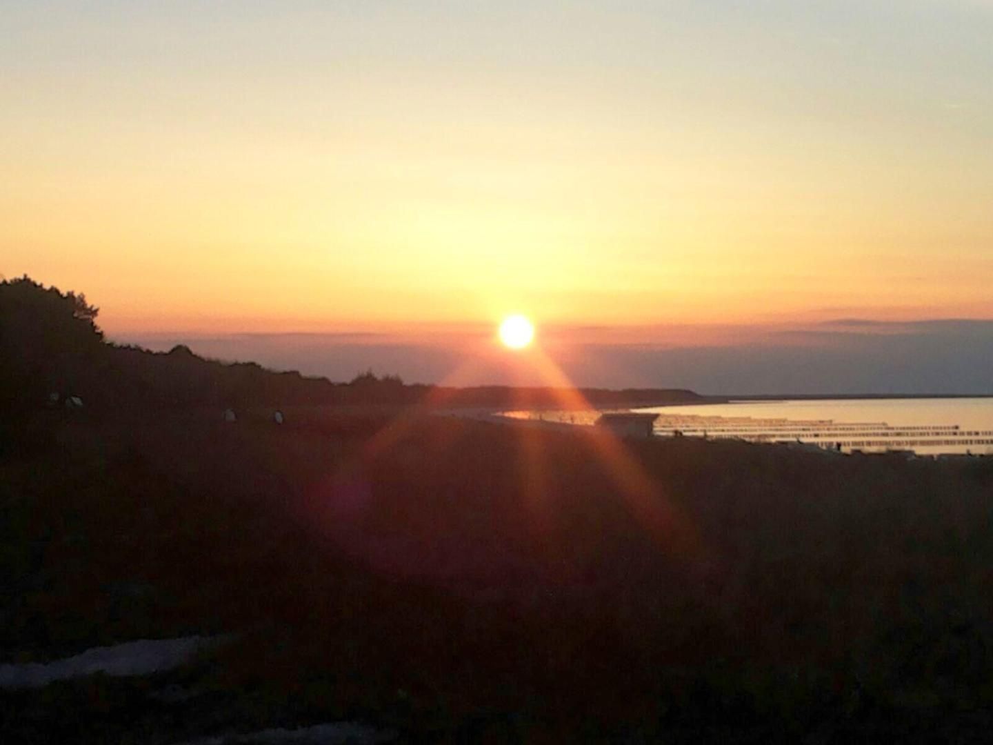 A sunset over a body of water with a distant shoreline and a pier extending into the water.