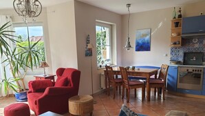 Ein Wohnzimmer mit einem roten Sessel, einem Esstisch mit Stühlen, einer Küche mit blauen Schränken und einem großen Fenster.