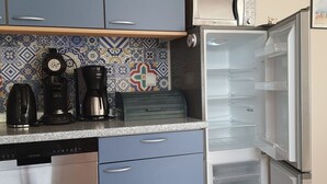 Eine kleine Küche mit blauen Schränken, einer Kaffeemaschine, einem Toaster und einem Kühlschrank.