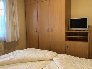 Ein Schlafzimmer mit Bett, Holzschrank und Fernseher auf einem Regal.